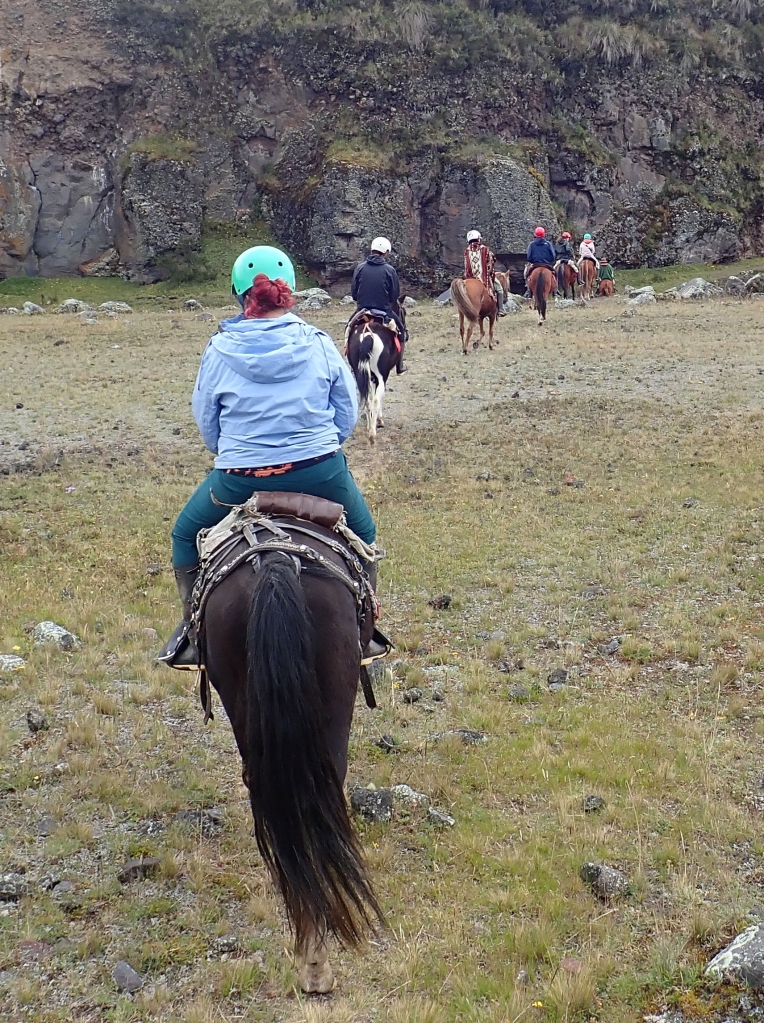 Photo of a line of 5 riders on horses walking across an open plain with a cliff in front of them