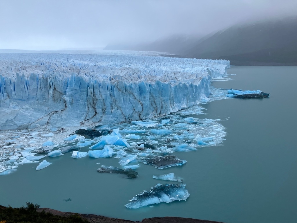 photo of a wide field of jagged glacial ice with deep blue and white shatter icebergs in the lake in front
