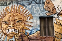photo of a wall mural around a grated window depicting an angry woman with a white kerchief on her head shaking her fist at an angry sun